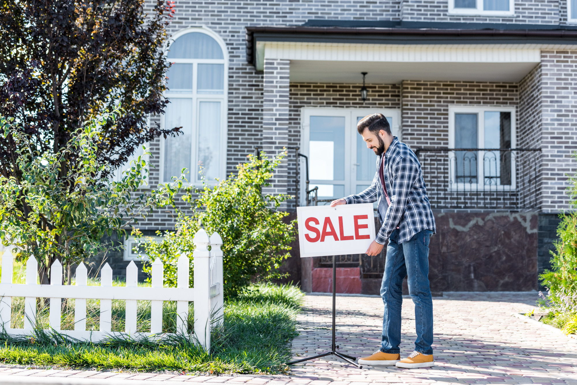 man with sale sign in front of home